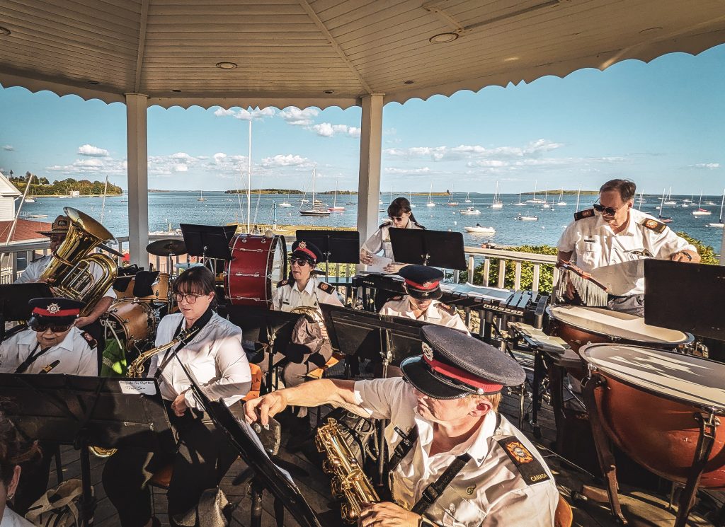 The BFD Band playing at chester bandstand in front of a blue sky and sailboats on the water